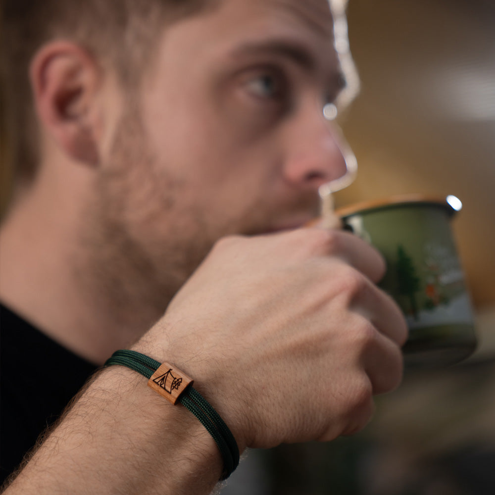 Verstellbares Outdoor-Armband aus dunkelgrünem Segeltau mit Holzschieber und Camping-Gravur (Zelt im Wald) mit Schiebeverpackung.