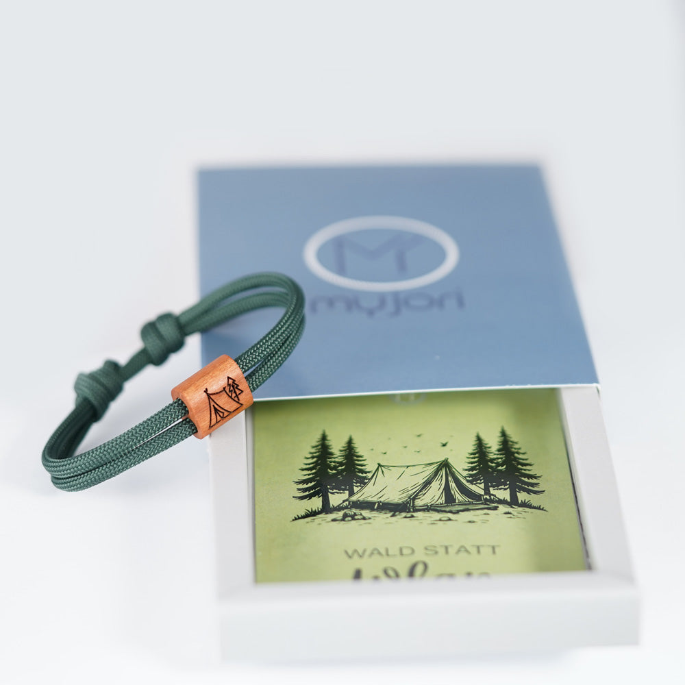 Verstellbares Outdoor-Armband aus dunkelgrünem Segeltau mit Holzschieber und Camping-Gravur (Zelt im Wald) mit Schiebeverpackung.
