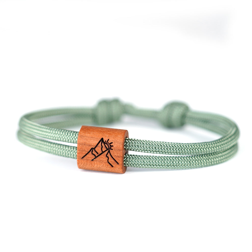 Verstellbares Outdoor-Armband aus grünem Segeltau mit Holzschieber und Berggipfel Motiv Gravur mit Schiebeverpackung.